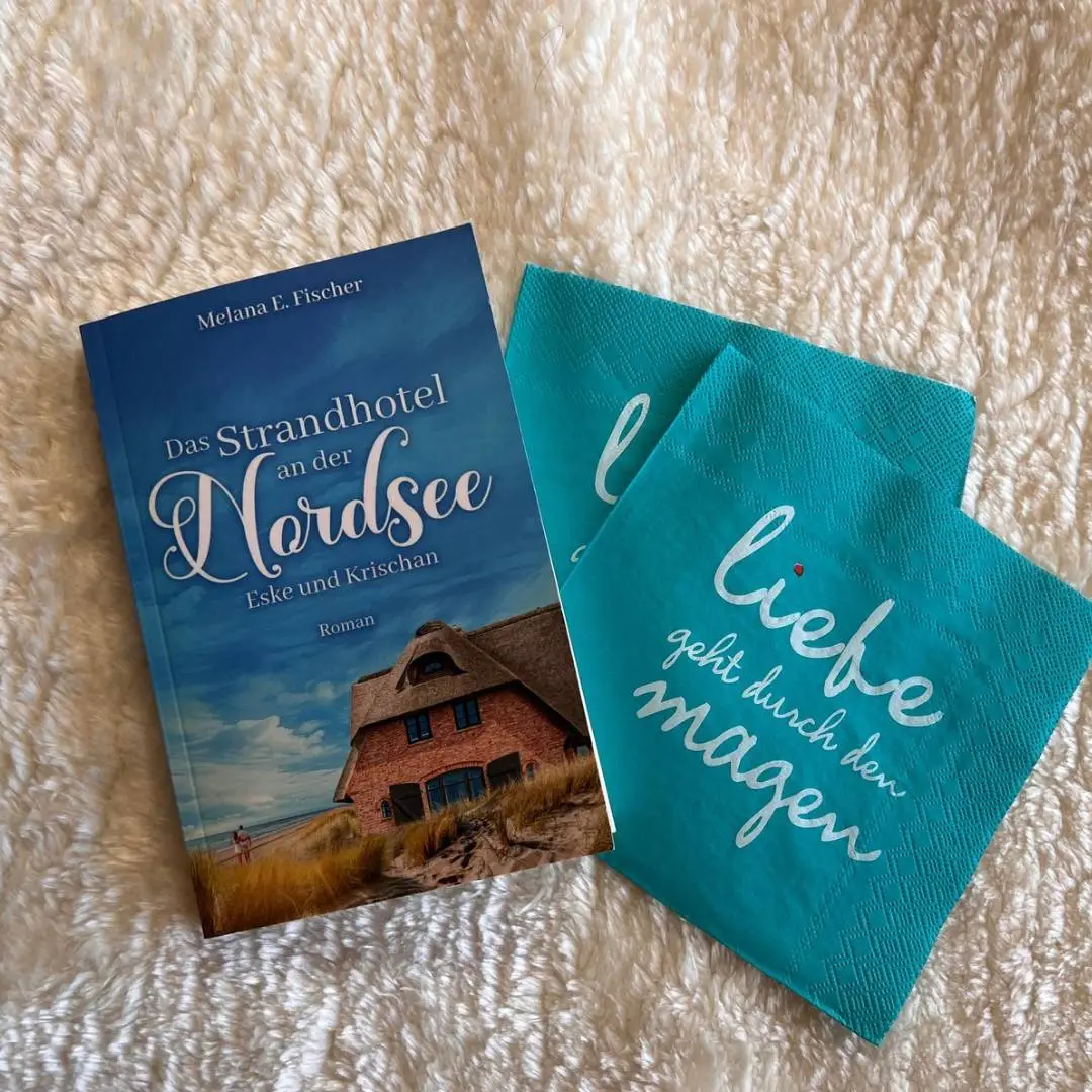 13.08.2024: News - Out Now - Das Taschenbuch zur Reihe Das Strandhotel an der Nordsee heller Flusenteppich,
darauf das Buch Das Strandhotel an der Nordsee mit 2 Servietten mit Liebe geht durch den Magen